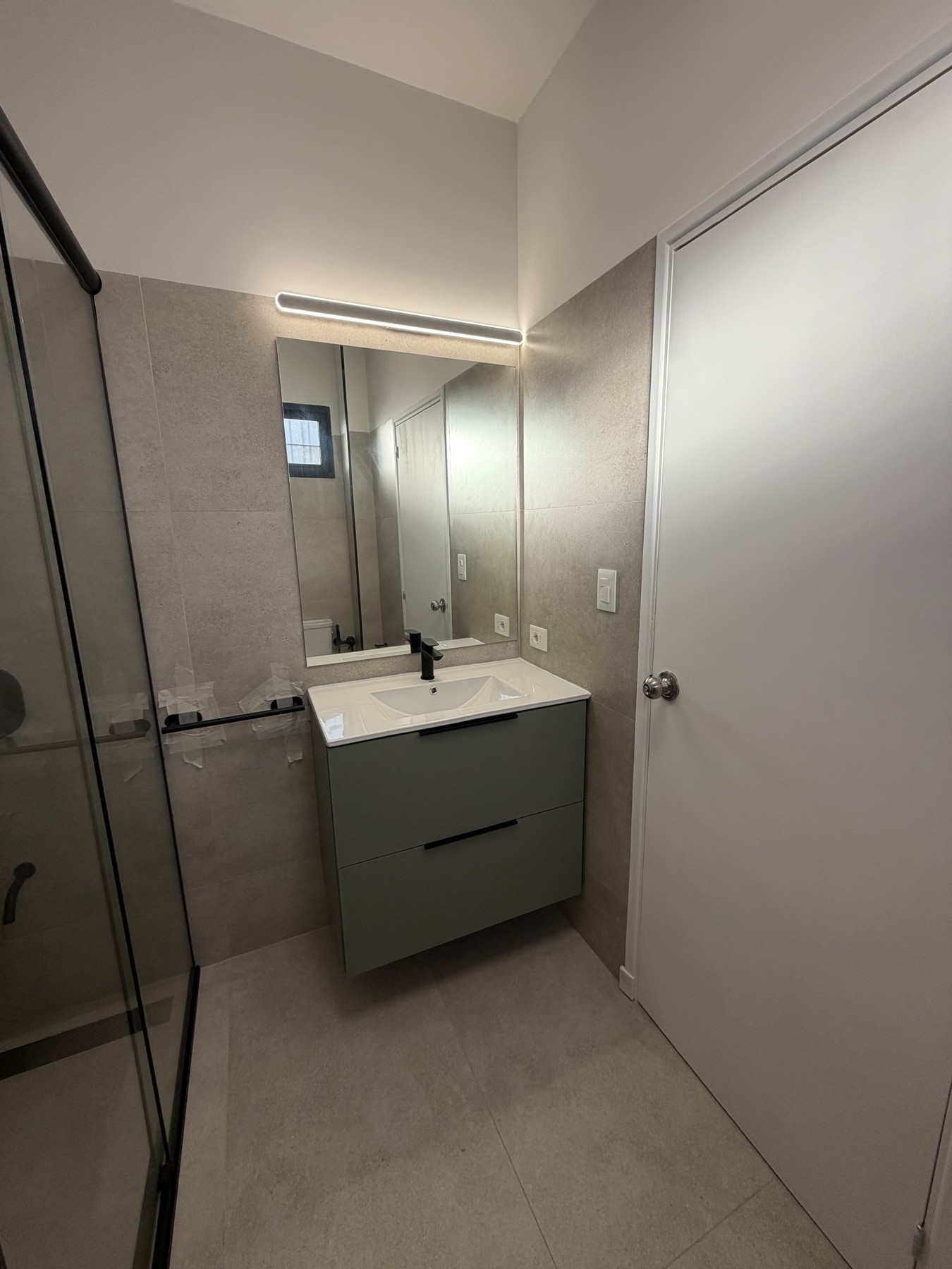 Reforma de baño con mueble suspendido verde, espejo amplio y revestimientos grises claros