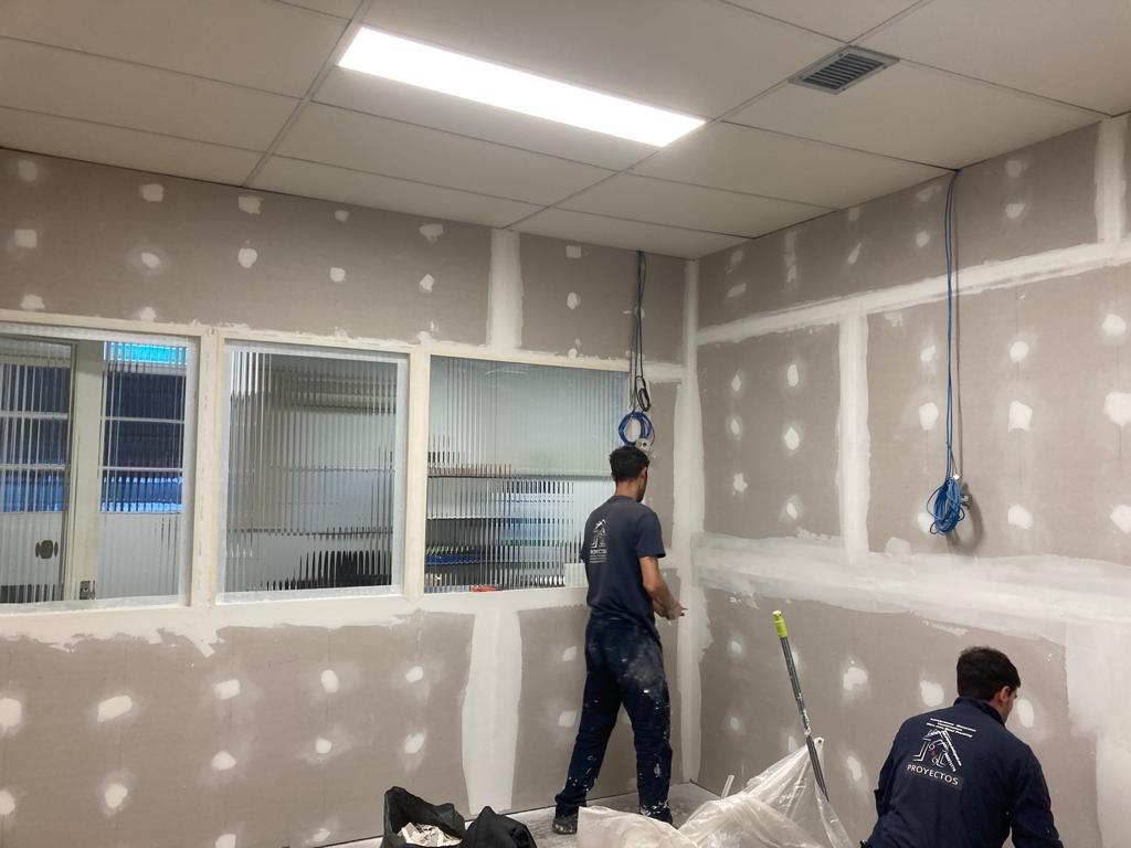 Trabajadores uniformados preparando juntas de placas de yeso en paredes de oficina